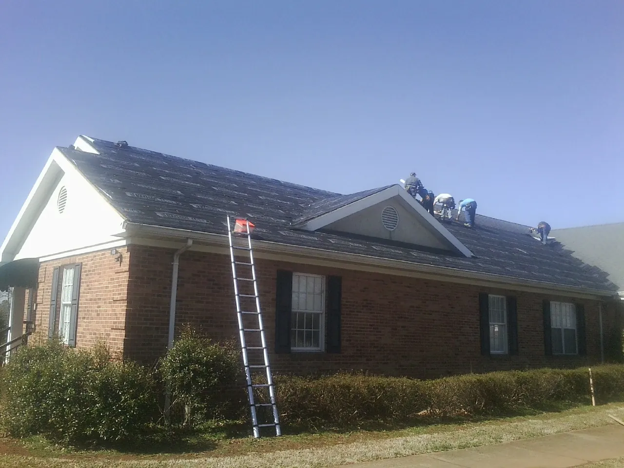 Crew tearing shingles off a brick ranch roof with a ladder set — Emergency Roof Repair work by our crew in Royersford