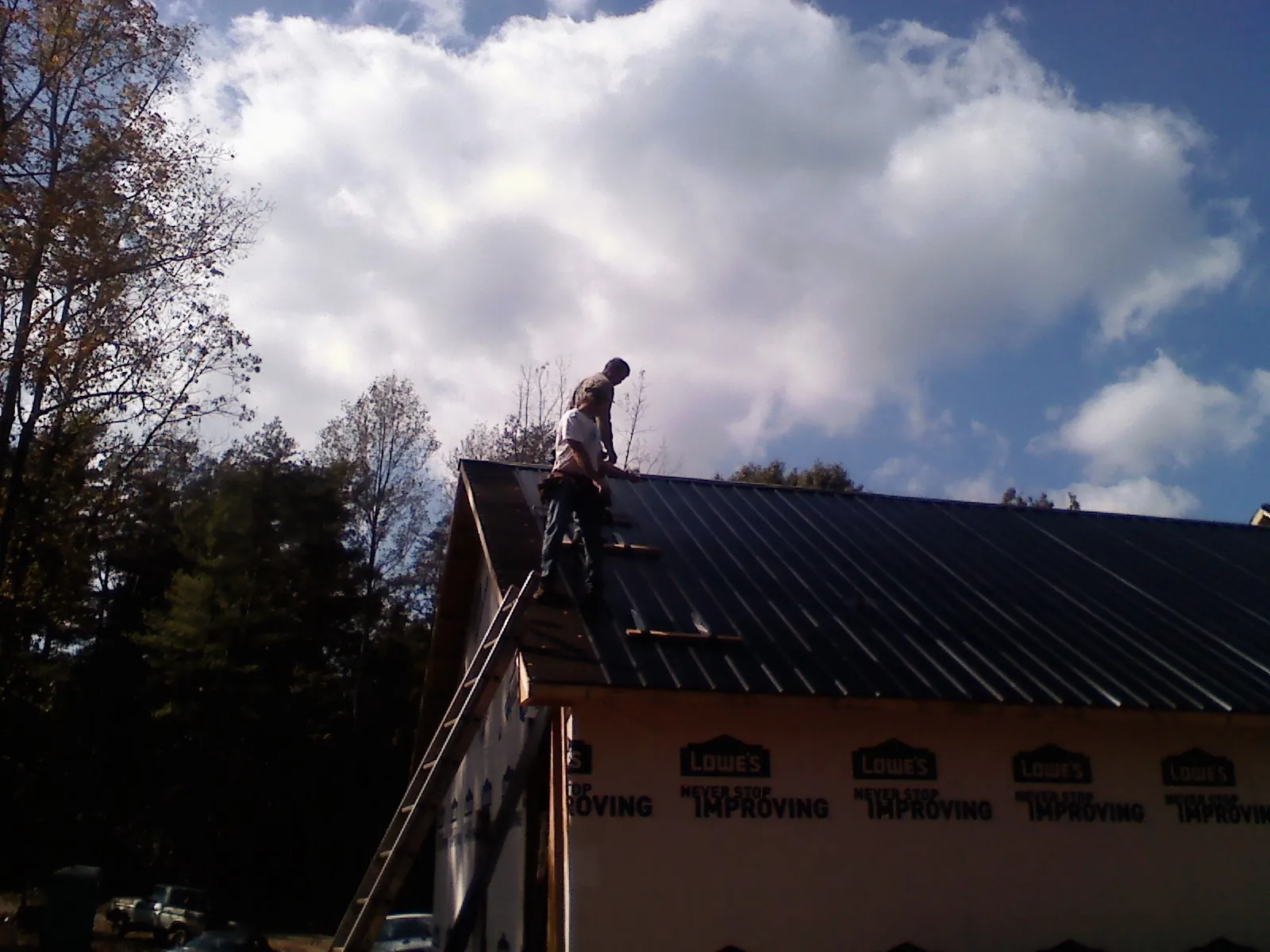Roofer fastening dark metal panels high against a cloudy sky, from a Roof Inspection job in Royersford