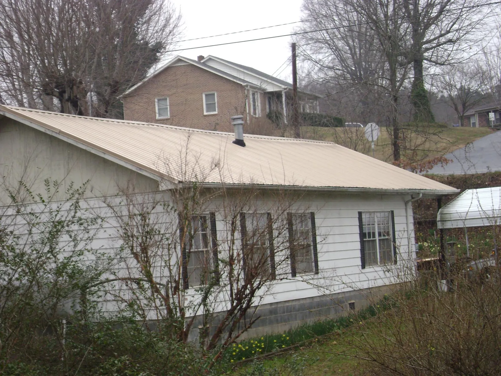 Tan metal roof on a white sided house set into a hillside — Commercial Roofing by Roofing Brothers in Royersford